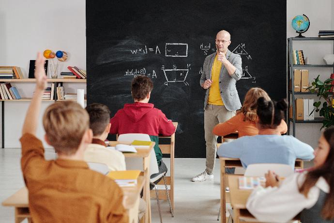 Nauczyciel stojący przed tablicą udzielający głosu jednego z sześciu uczniów