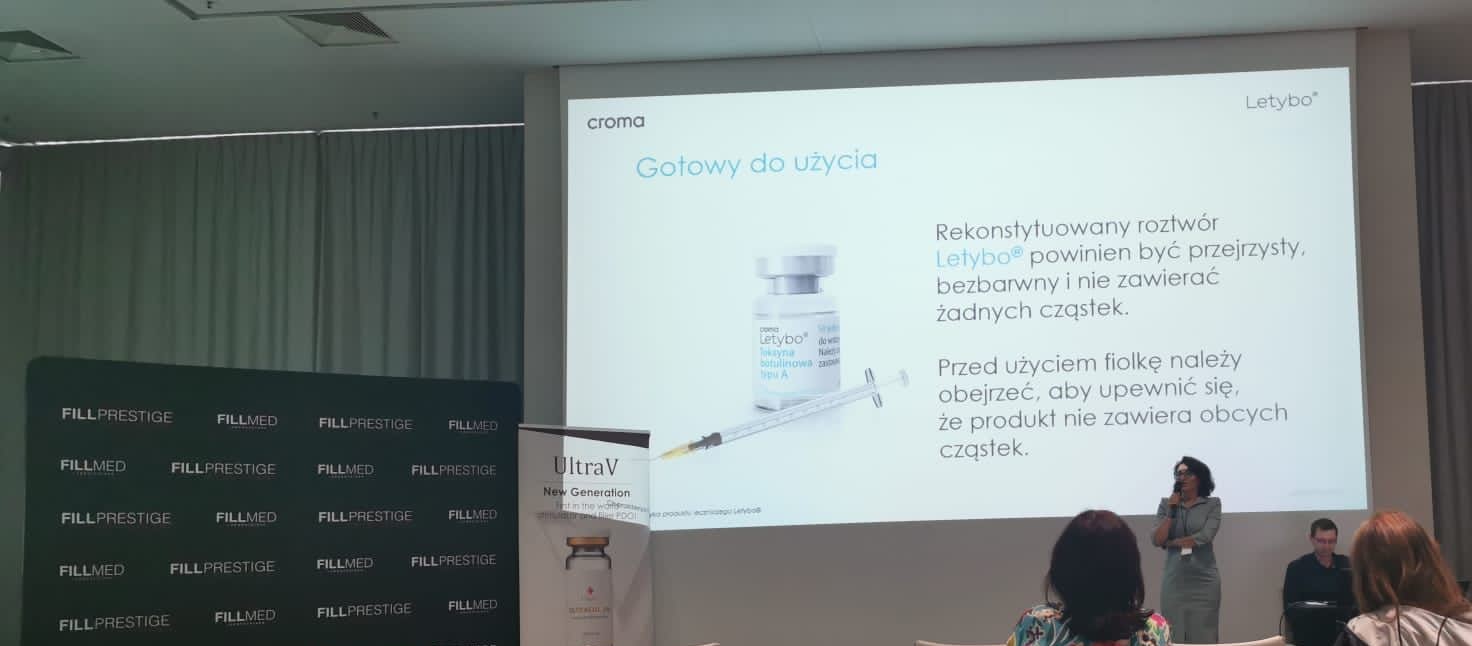 Zdjęcie przedstawiające kobietę wygłaszającą wykład, w tle prezentacja i słuchacze